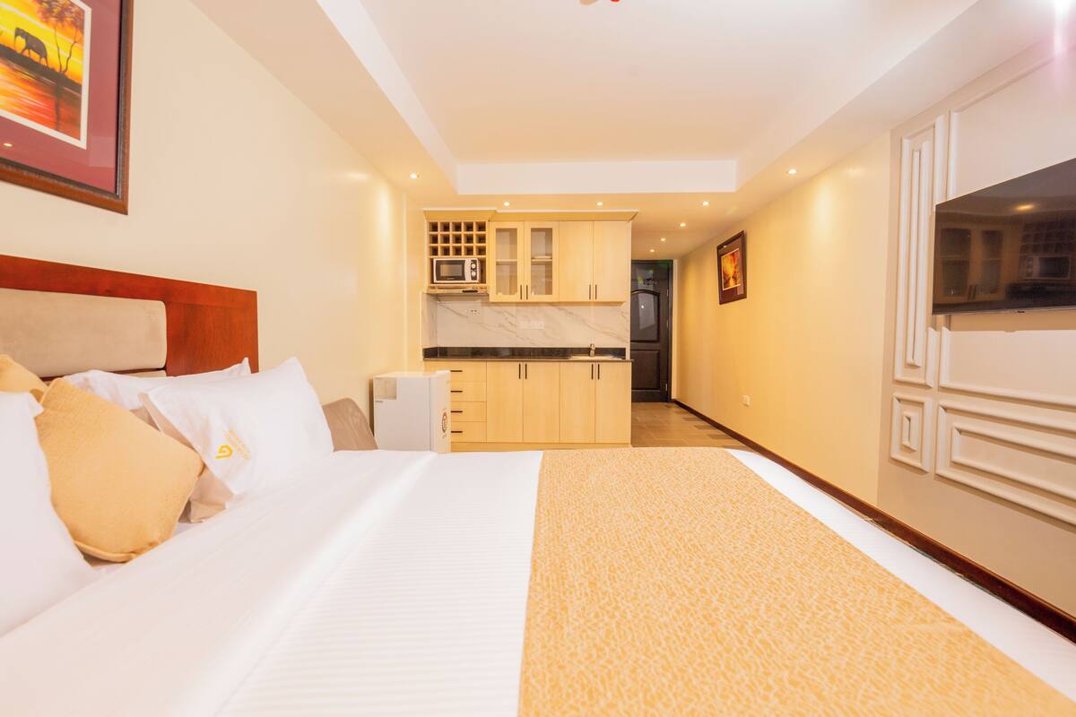 A hotel room with a bed, a small kitchenette, and a TV.