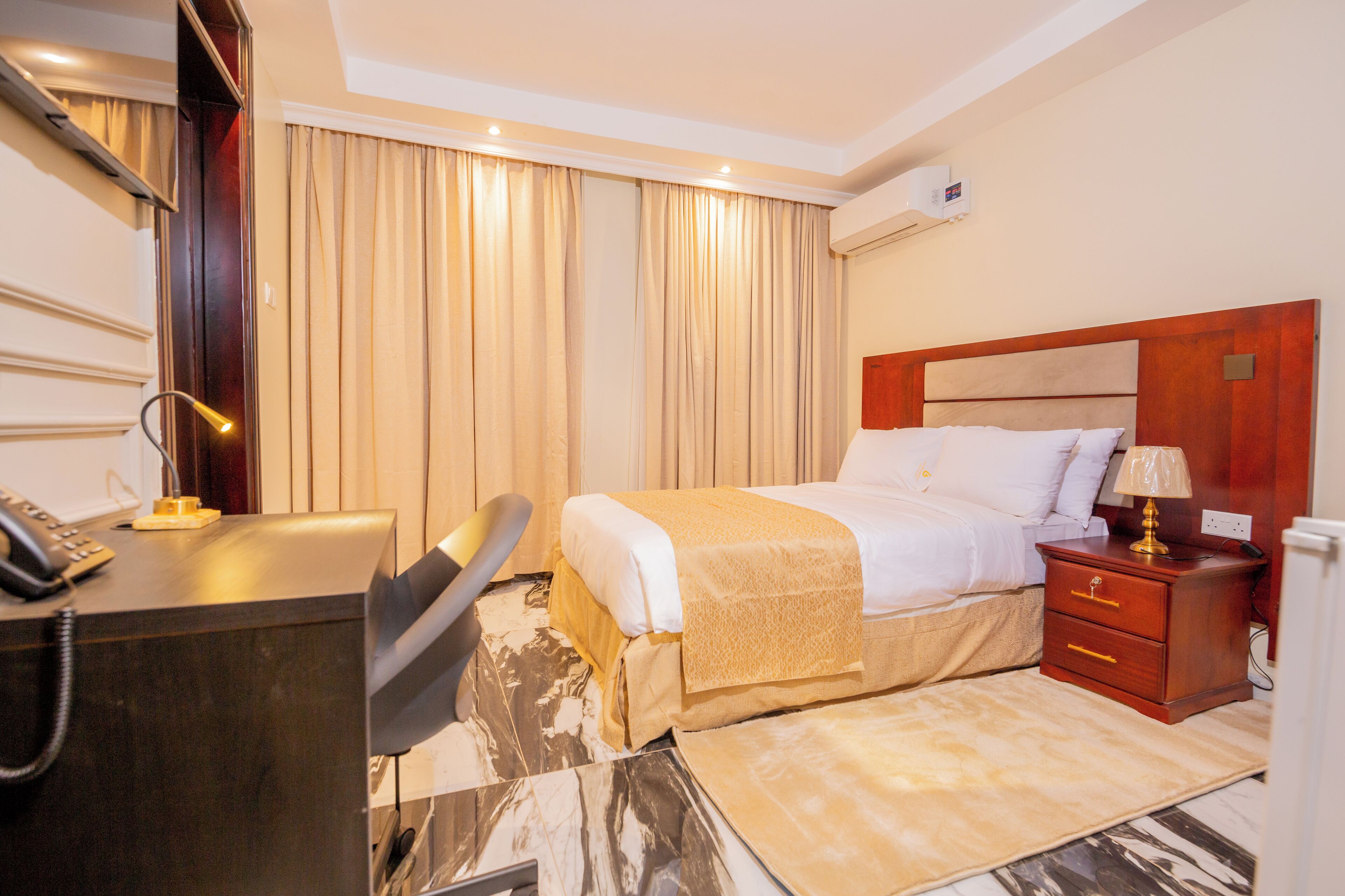 A hotel room with a bed, bedside table, desk with a telephone, and a chair.