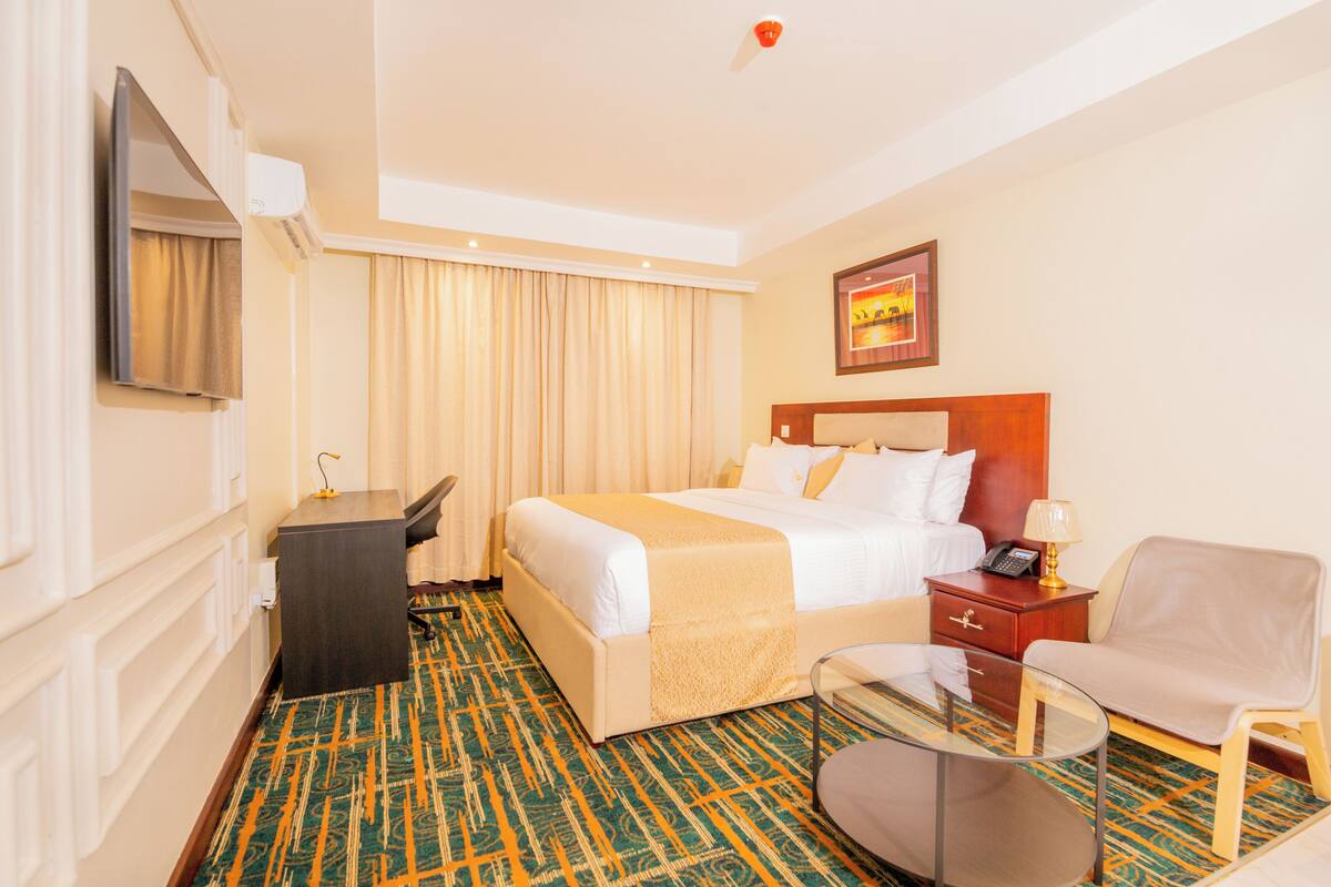 A hotel room with a bed, bedside table, chair, desk, and a television.