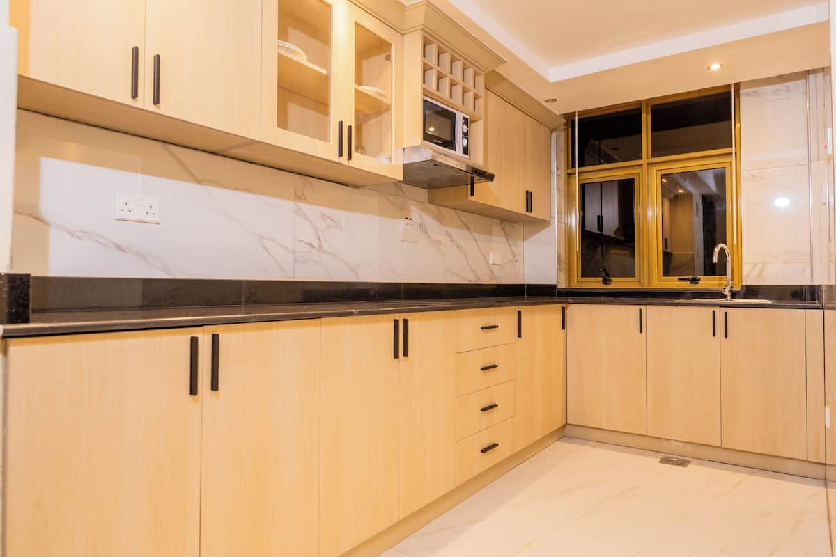 A modern kitchen with wooden cabinets, a black countertop, and a built-in microwave.