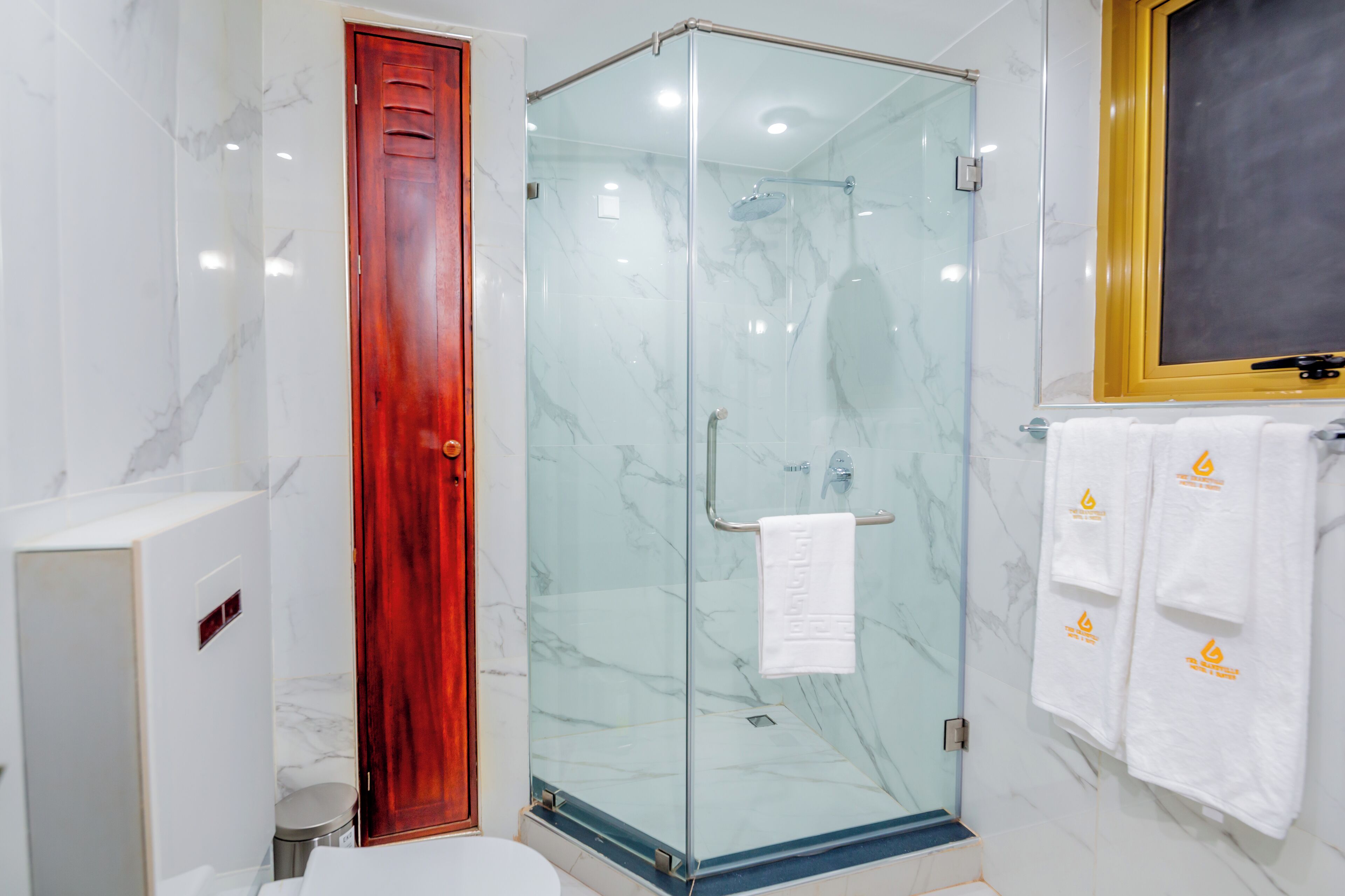 Un baño moderno con cabina de ducha de vidrio, puerta de madera y toallero con toallas blancas.
