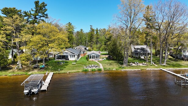 A lakeside property with multiple houses, a dock, and a boat. - Loon Lodge - Super Cute, Lakefront, Bonfire Ring, and Private Dock! (Oscoda)