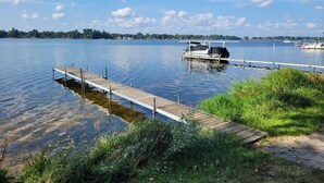 A wooden dock extending into a calm lake with boats docked at the pier. - Loon Lodge - Super Cute, Lakefront, Bonfire Ring, and Private Dock! (Oscoda)