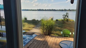 A wooden deck with a view of a lake, a green chair, and a small table. - Loon Lodge - Super Cute, Lakefront, Bonfire Ring, and Private Dock! (Oscoda)