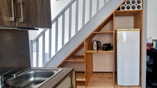 A kitchen with a wooden cabinet, a stainless steel sink, and a built-in wooden shelf with a white refrigerator.