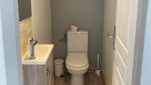 A compact bathroom with a toilet, a sink, and a small shelf with decorative items.