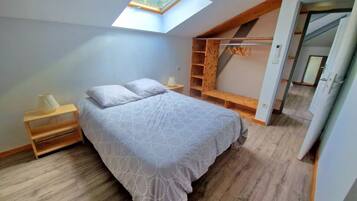 Une chambre avec une lucarne, un lit recouvert d’une literie à motifs, une table de chevet en bois et une étagère intégrée en bois.