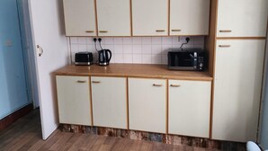 Una cocina compacta con armarios blancos, un microondas, un tostador y una tetera.