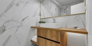 A bathroom with a marble wall, a wooden vanity, a white sink, and a mirror with a gold frame. - 04. Luxury Apartments L&L in Tucepi (Tucepi)