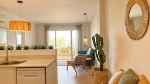 A modern kitchen with a built-in dishwasher, a dining area with a blue sofa and a cactus plant, and a large mirror on the wall. - Apartamento Miramar (Denia)