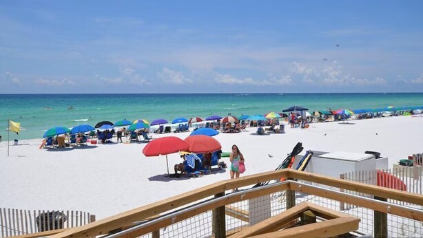 A beach with umbrellas and beach chairs, a wooden deck, and a clear view of the ocean.
