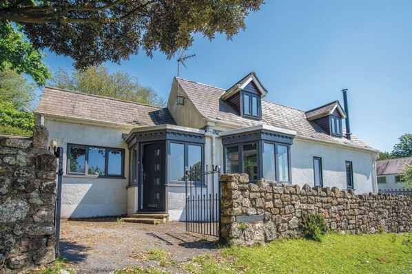 A two-story house with a stone wall, a black gate, and a clear sky.