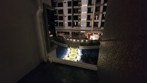 A nighttime view of a building's interior with a balcony overlooking a pool area.
