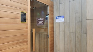 A sauna entrance with wooden walls and a glass door. There are signs indicating safety instructions and a notice to use the sauna properly.