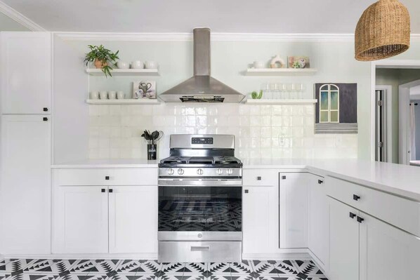 A modern kitchen with white cabinets, a stainless steel range hood, and a patterned floor.