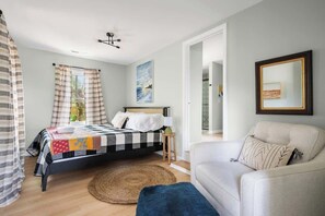 A bedroom with a bed, a bedside table, a chair, a large mirror, and a view of the outdoors.
