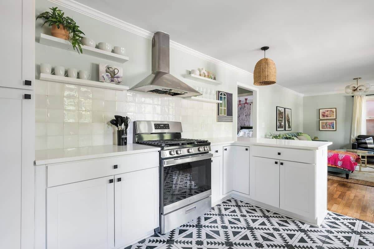 Een moderne keuken met witte kastjes, een roestvrijstalen fornuis en een hanglamp.