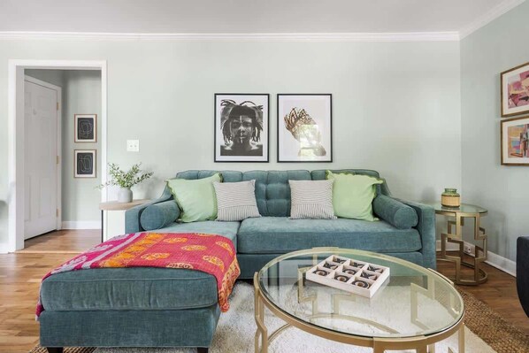 A living room with a teal sofa, a glass coffee table, and a colorful throw blanket.