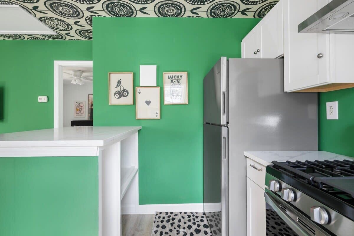 A kitchen with green walls, a refrigerator, a stove, and framed pictures on the wall.