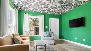 Una stanza con pareti verdi, un divano marrone, una poltrona grigia, un tappeto decorato e un soffitto con un motivo circolare.