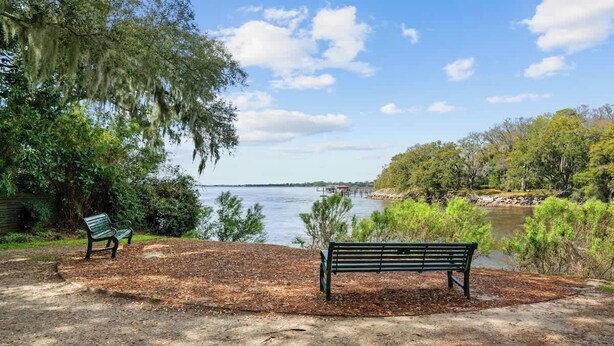 Un parco con due panchine, uno specchio d'acqua e una zona boschiva.