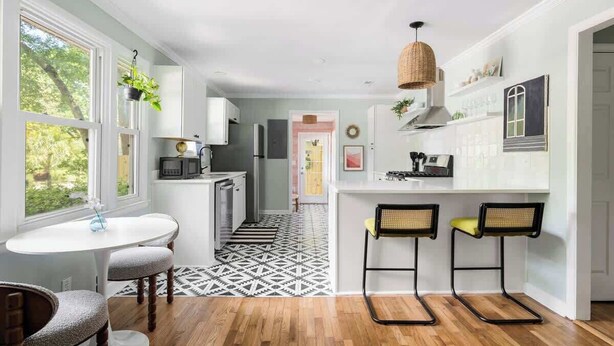 A modern kitchen with a dining area, wooden flooring, and a view of the outdoors.