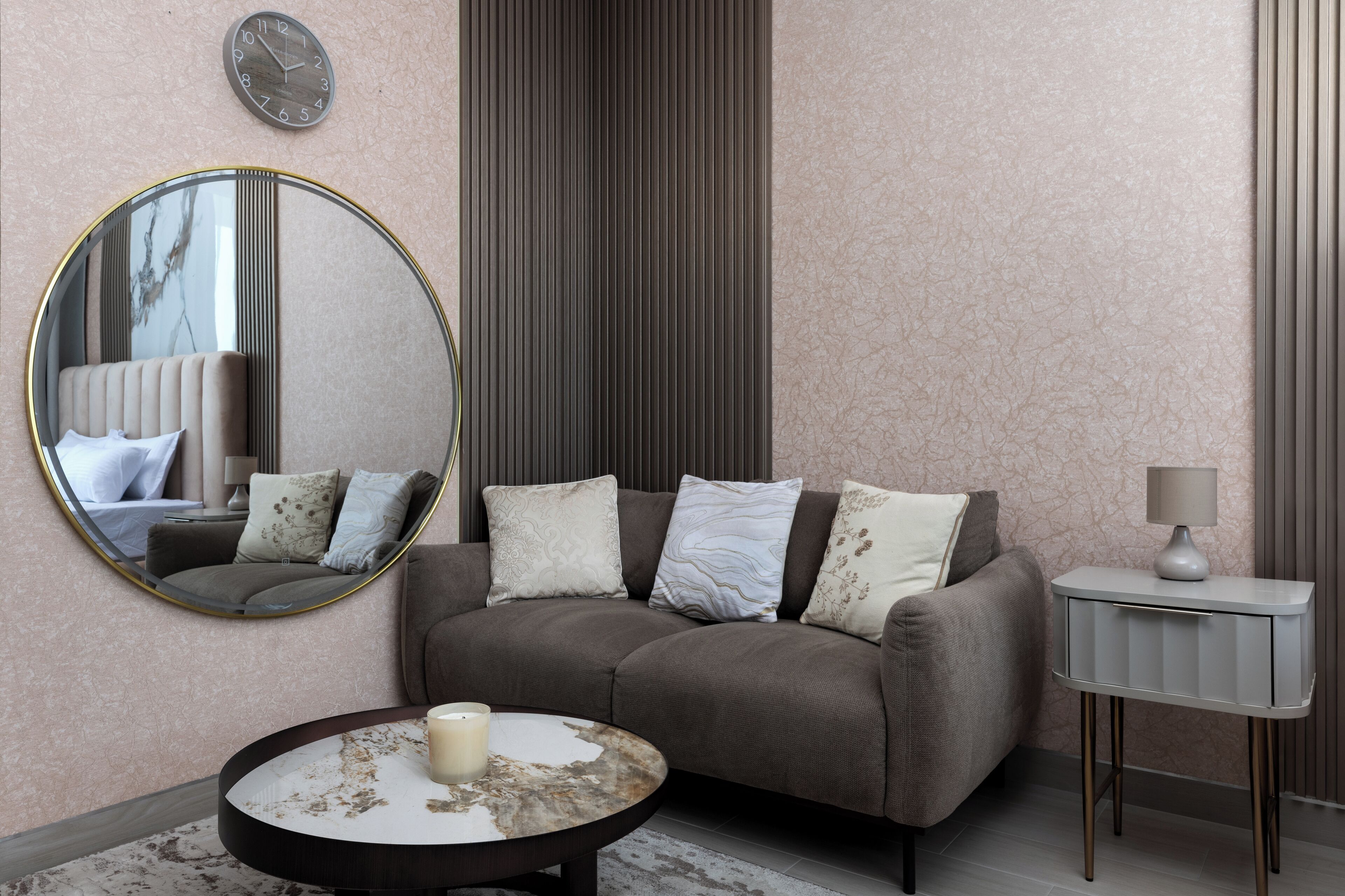 A modern living room with a sofa, a round coffee table, a side table, a mirror, and a clock on the wall.