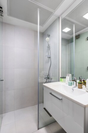 A modern bathroom with a glass shower enclosure, a white sink with a mirror, and toiletries on the counter. - Waves - Refined Studio with Balcony & City Views in Luma21 (Dubai)