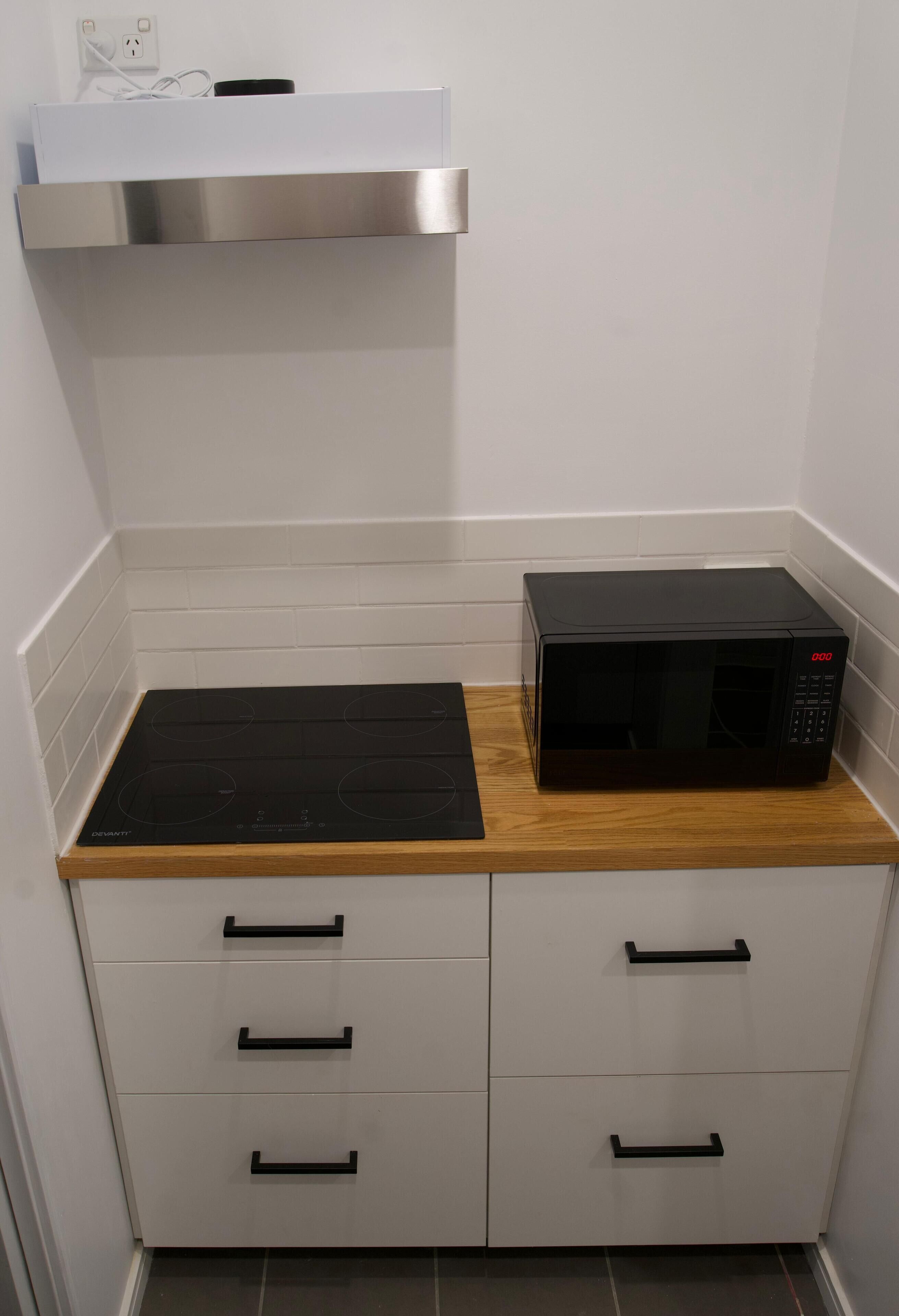 A compact kitchen with a black microwave, a stainless steel range hood, and a black induction cooktop.