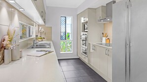 A modern kitchen with white cabinets, a stainless steel refrigerator, and a window with a view of greenery. - Palm Cove Studio Apartments (Palm Cove)