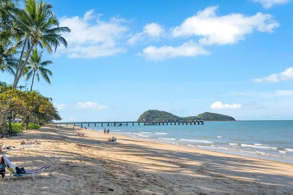 A beach with a pier extending into the water, palm trees, and a clear sky.