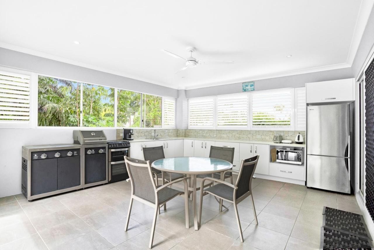 A modern kitchen with a round glass table, built-in appliances, and large windows offering a view of greenery.