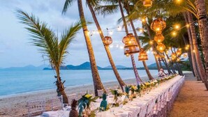 A beachside dining setup with tables and chairs, string lights, and palm trees. - Palm Cove Studio Apartments (Palm Cove)