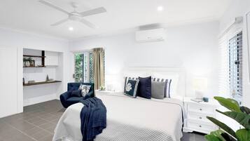 Un dormitorio moderno con cama, una silla, mesita de noche y ventilador de techo.