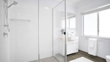 Um banheiro moderno com box de vidro, azulejos brancos, um espelho grande e uma janela que oferece iluminação natural.
