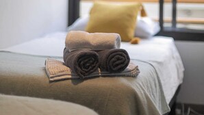 Una habitación de hotel con una cama, un ventanal con vista a un edificio y un cuadro enmarcado en la pared.