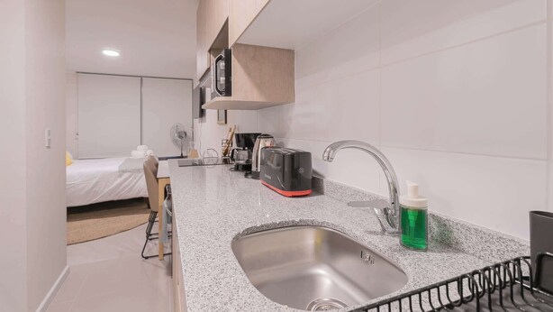 A compact hotel room with a kitchenette, a bed, a small table, and a chair.