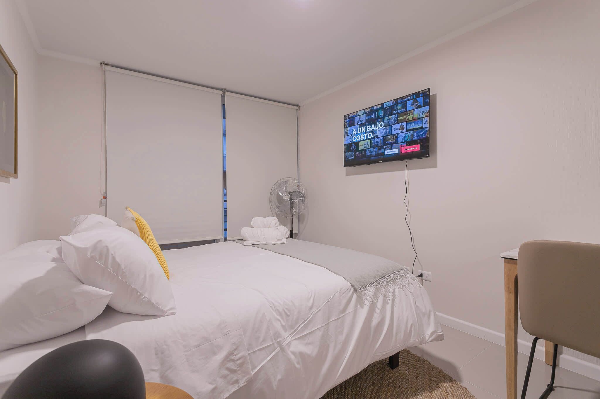 Une chambre d’hôtel équipée d’un lit, d’un téléviseur fixé au mur, d’un ventilateur et d’une chaise.