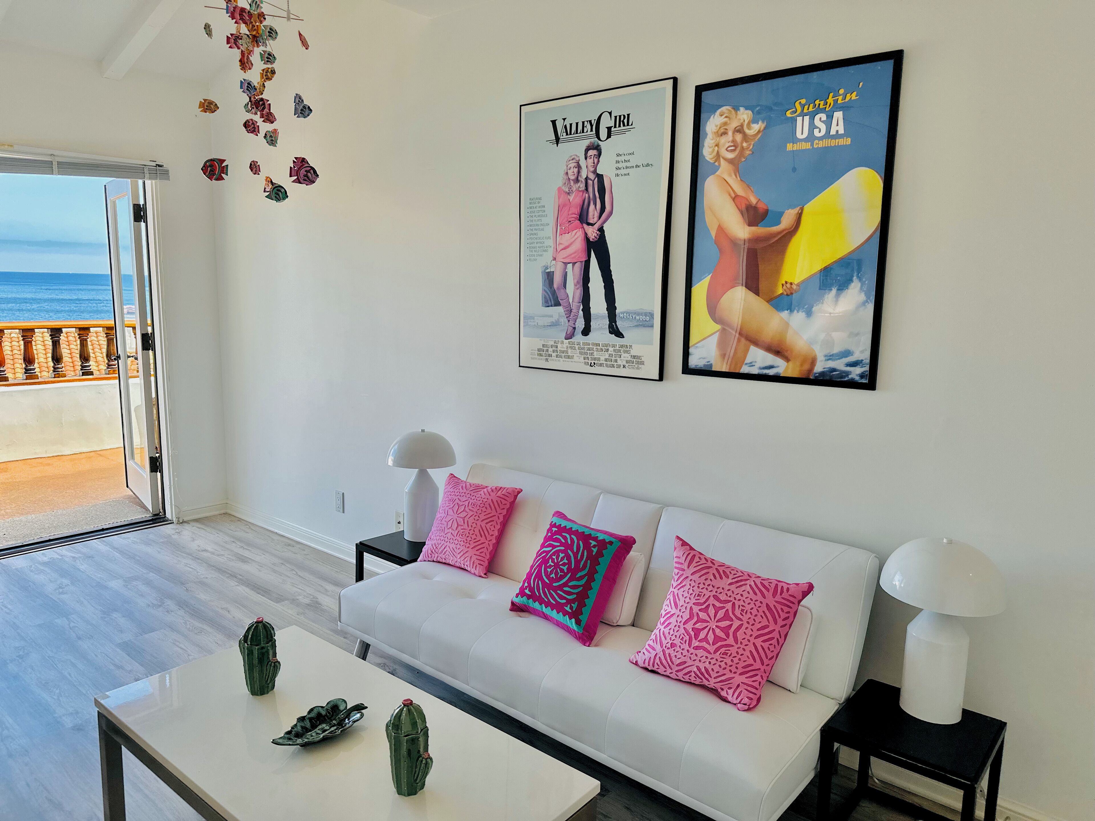 A modern living room with a white sofa, colorful pillows, a coffee table, and two framed posters on the wall.