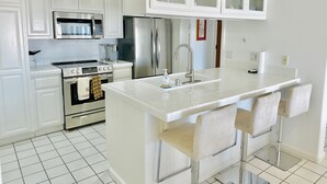 A modern kitchen with white cabinetry, stainless steel appliances, and a central island with bar stools. - Hamilton Cove Villa 9 58 With Zero Steps (Avalon)