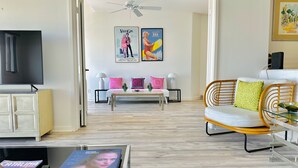A modern living room with a sofa, a coffee table, and a TV. There is a ceiling fan and artwork on the wall. - Hamilton Cove Villa 9 58 With Zero Steps (Avalon)
