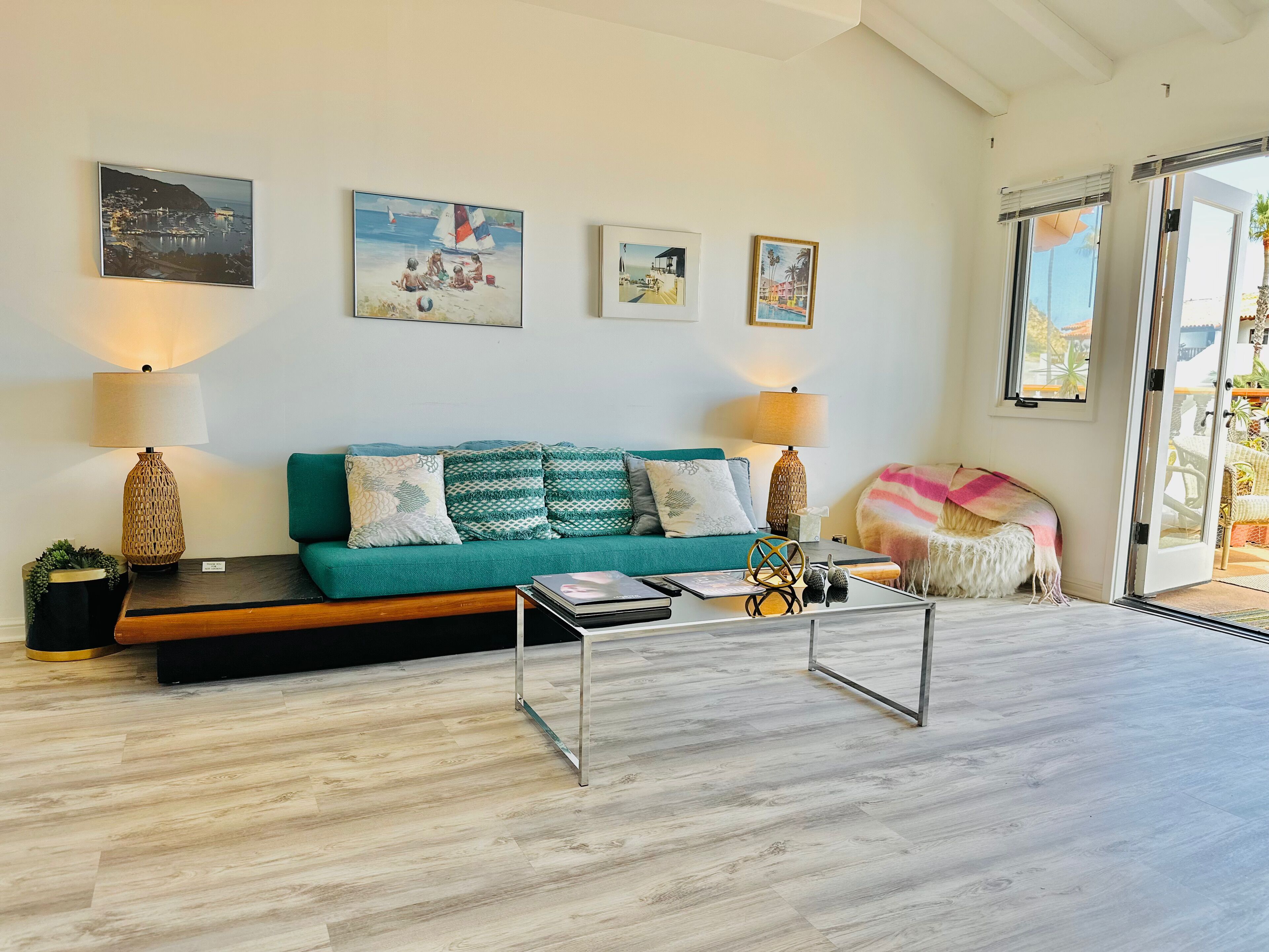 Una sala de estar moderna con un sofá color turquesa, dos lámparas, una mesa de centro y vistas al exterior a través de un ventanal corredero.