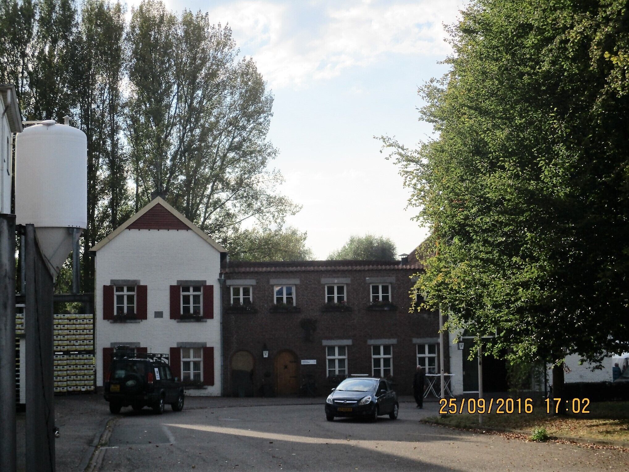 Ein Gebäude mit weißer Fassade und roten Fensterläden, ein geparktes Auto und ein Lastwagen davor.