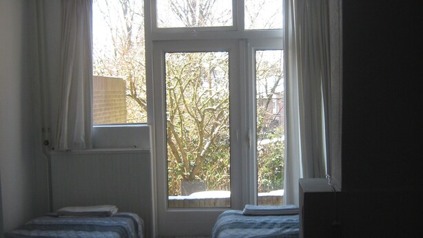 A room with two beds, a window with curtains, and a radiator. - House Rumpen 10 single beds 7 bedrooms with hot and cold water Brunssum  (Brunssum)
