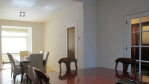 A dining area with a wooden table and chairs, a window with blinds, and a door with a textured panel. - House Rumpen 10 single beds 7 bedrooms with hot and cold water Brunssum  (Brunssum)
