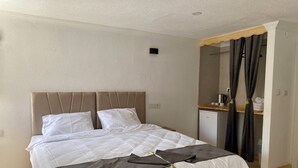 A neatly made bed with a headboard, a small kitchenette area with a coffee machine, and a bathroom with a shower curtain. - Bak cafe& pansiyon (Ayvalik)