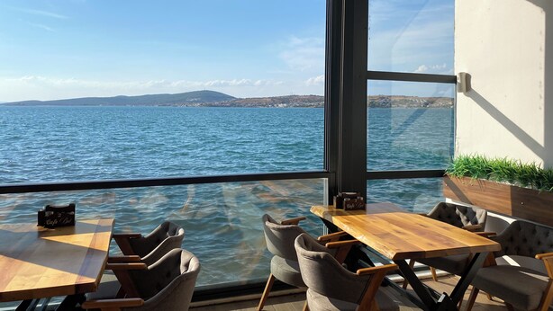 A terrace with a view of the sea, wooden tables, and chairs. - Bak cafe& pansiyon (Ayvalik)