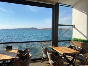 A terrace with a view of the sea, wooden tables, and chairs. - Bak cafe& pansiyon (Ayvalik)