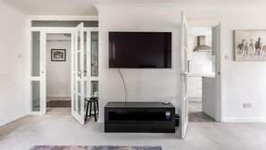 A living room with a flat-screen TV mounted on the wall, a black entertainment unit, and a colorful rug. - Spacious 1 bed Apartment With Parking & Balcony! (Bromley)