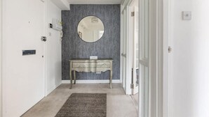 A hallway with a grey textured wall, a round mirror, a wooden console table with a sign, and a carpeted floor. - Spacious 1 bed Apartment With Parking & Balcony! (Bromley)